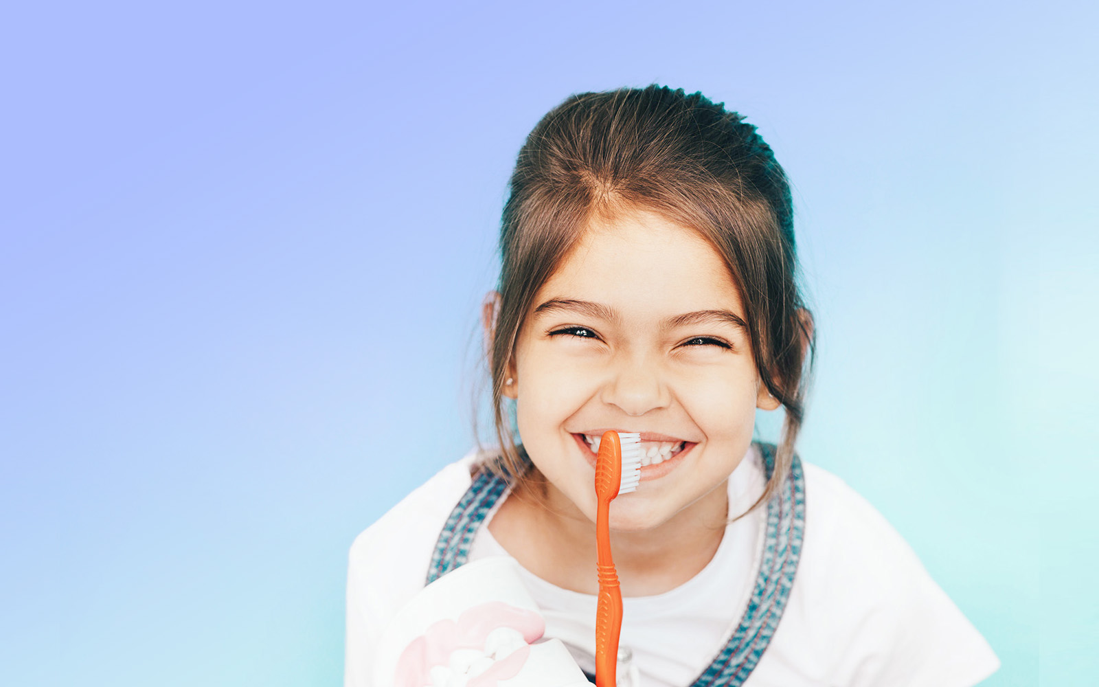 The image shows a young girl with a joyful expression, brushing her teeth with a toothbrush.