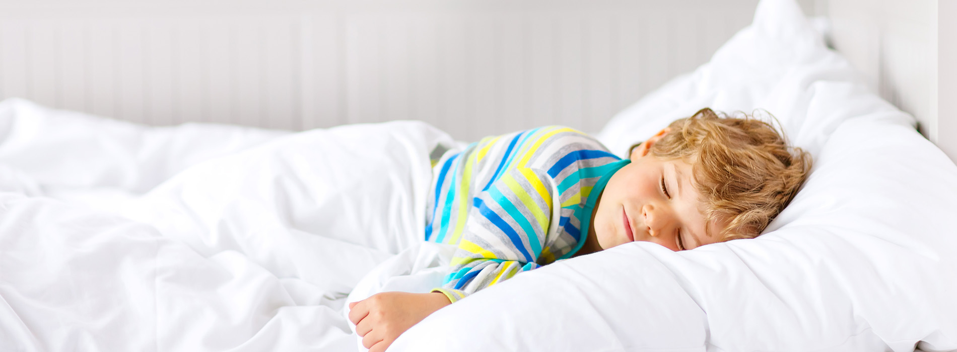 A young child sleeping in a bed with white sheets.