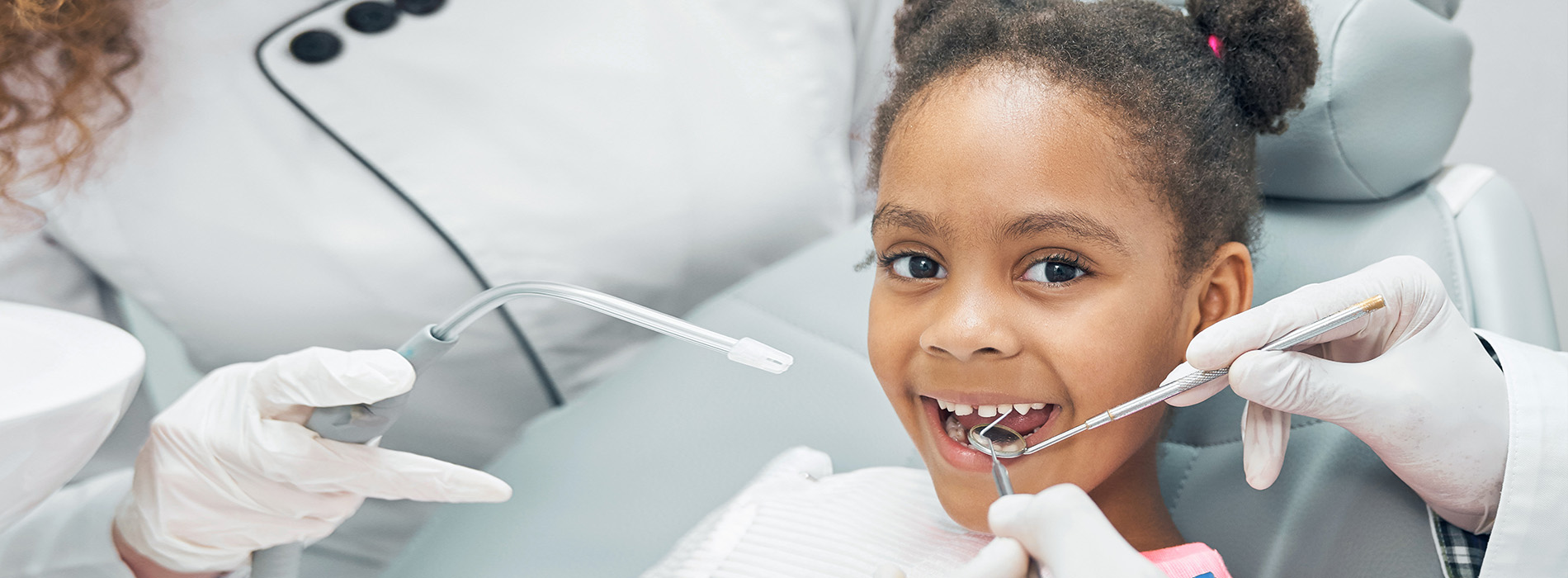 A young child receiving dental care in a professional setting, with a dentist and dental hygienist attending to the child s needs.