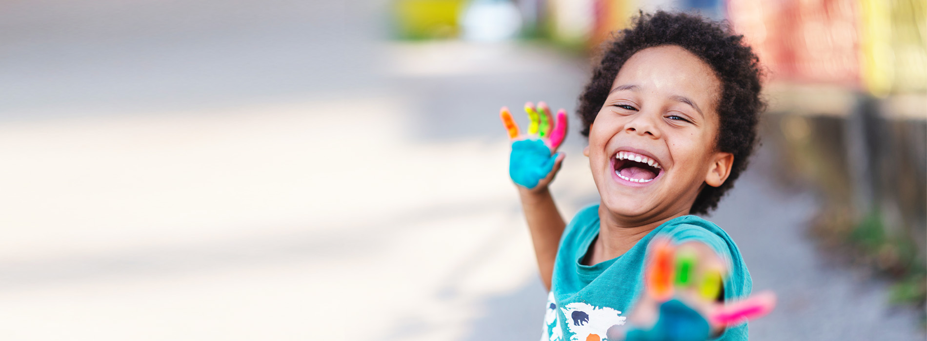 A young child is smiling and holding a colorful object, standing on a sidewalk.